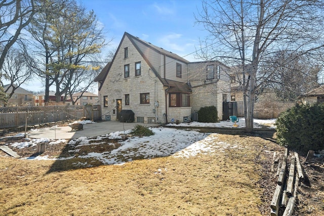 view of snow covered exterior featuring stone siding, a patio area, and fence