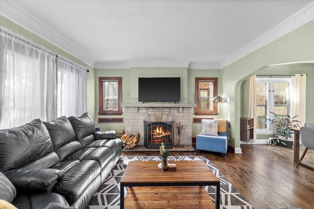 living area featuring ornamental molding, arched walkways, dark wood-style flooring, and a stone fireplace