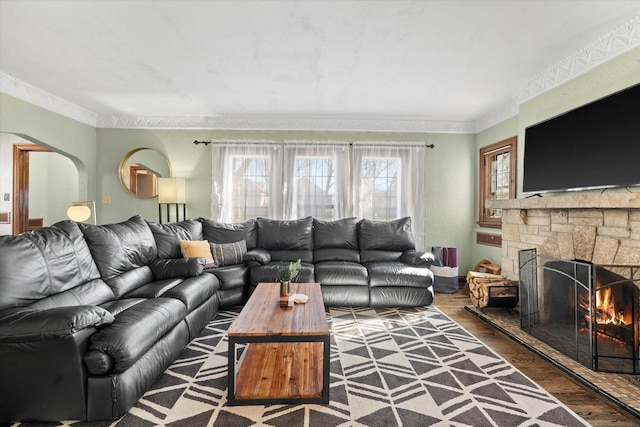 living room with crown molding, arched walkways, wood finished floors, and a stone fireplace