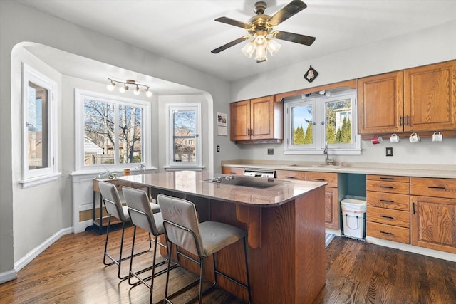 kitchen with a breakfast bar, dark wood-style flooring, brown cabinets, and a sink