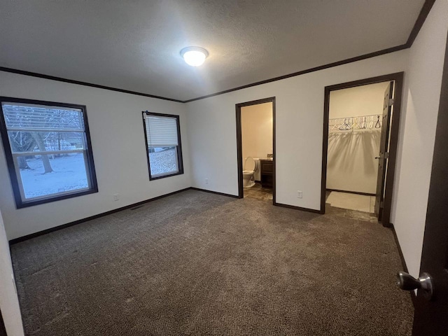 unfurnished bedroom with a textured ceiling, connected bathroom, baseboards, ornamental molding, and dark carpet