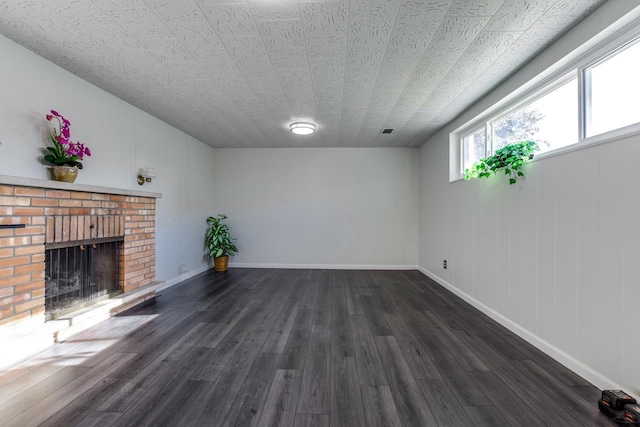 unfurnished living room with dark wood-style floors, a brick fireplace, and baseboards