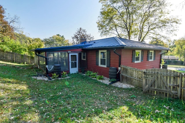 view of front of property featuring a chimney, a sunroom, metal roof, fence, and a front lawn