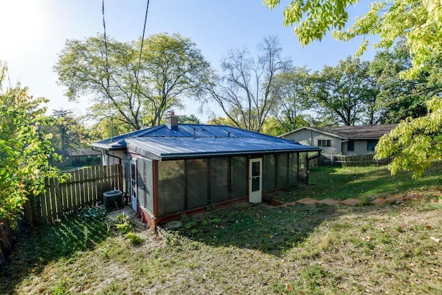 rear view of property featuring a fenced backyard, metal roof, a chimney, and central AC unit