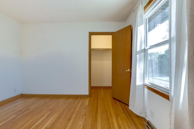 unfurnished bedroom with light wood finished floors, a closet, a walk in closet, and baseboards