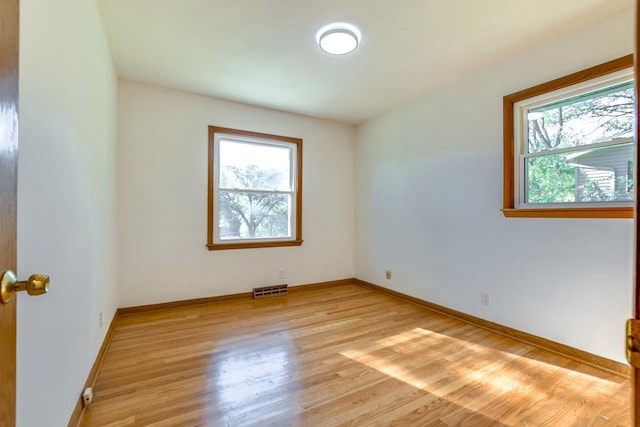 empty room featuring a healthy amount of sunlight, light wood finished floors, baseboards, and visible vents