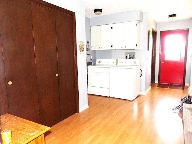 clothes washing area featuring light wood-style floors, baseboards, cabinet space, and washing machine and clothes dryer