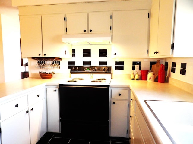 kitchen featuring white cabinets, light countertops, under cabinet range hood, and decorative backsplash