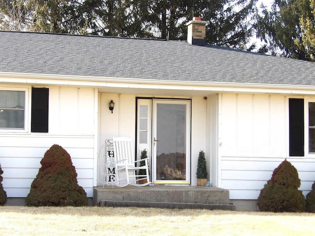 view of exterior entry with a chimney and roof with shingles