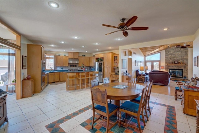 dining area with a ceiling fan, recessed lighting, a stone fireplace, light tile patterned floors, and vaulted ceiling