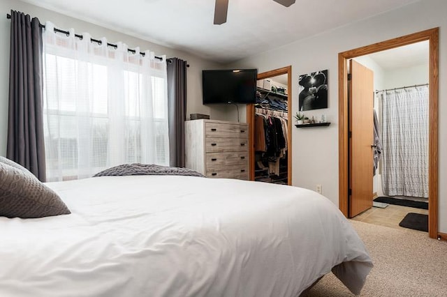 bedroom with light carpet, a ceiling fan, ensuite bathroom, a spacious closet, and a closet