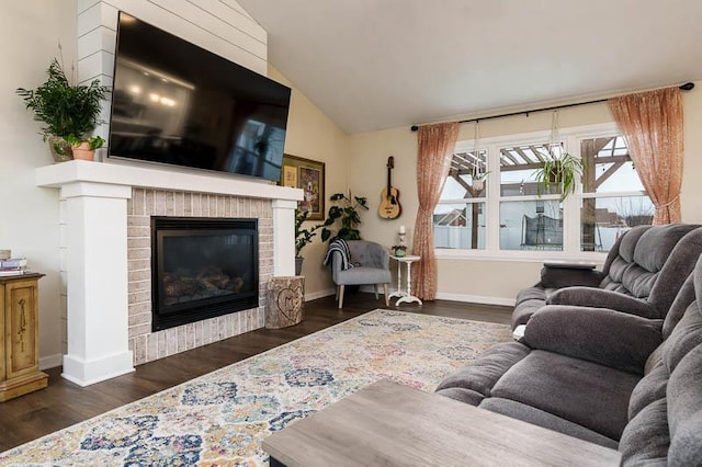 living room featuring lofted ceiling, a brick fireplace, baseboards, and dark wood-style flooring