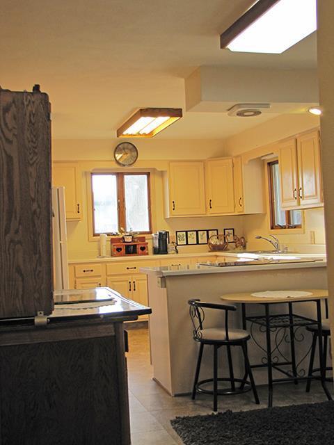872 Northside Dr, Platteville, WI 53818 - kitchen featuring a peninsula, white cabinetry, light countertops, freestanding refrigerator, and a kitchen bar