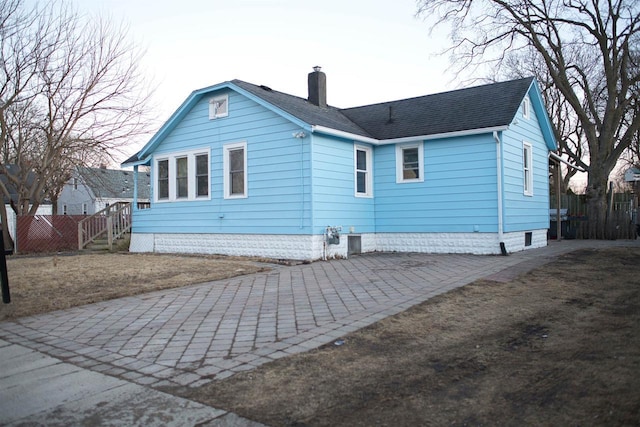 back of house featuring a shingled roof, a chimney, and fence