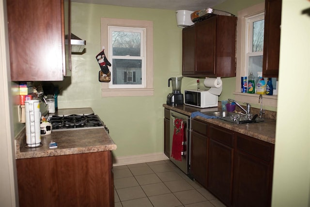 kitchen featuring stainless steel dishwasher, white microwave, a sink, dark tile patterned flooring, and baseboards