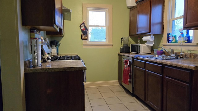 kitchen featuring dark countertops, white microwave, light tile patterned flooring, dishwasher, and baseboards