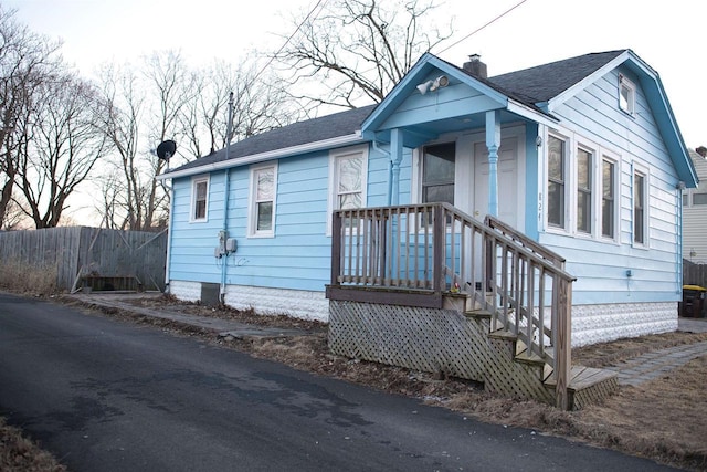 bungalow-style home with a shingled roof, fence, and a chimney