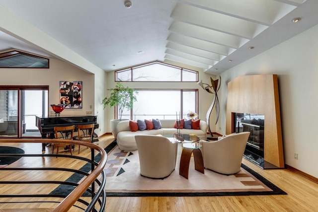 dining room featuring a glass covered fireplace, vaulted ceiling, light wood-style flooring, and a healthy amount of sunlight