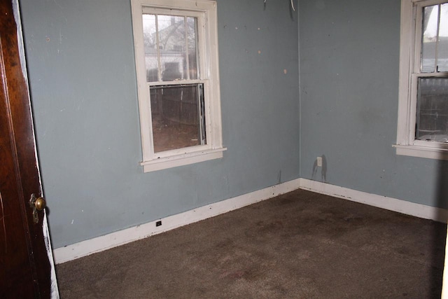 empty room featuring baseboards and dark colored carpet