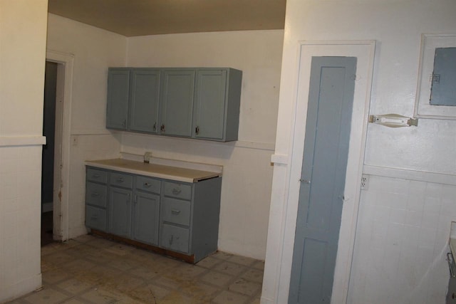 kitchen with a wainscoted wall, light floors, electric panel, and gray cabinetry