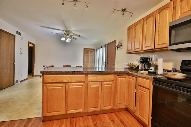 kitchen with black range with electric cooktop, a peninsula, stainless steel microwave, and dark countertops