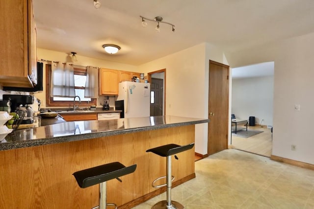 kitchen featuring baseboards, a kitchen breakfast bar, freestanding refrigerator, a peninsula, and a sink