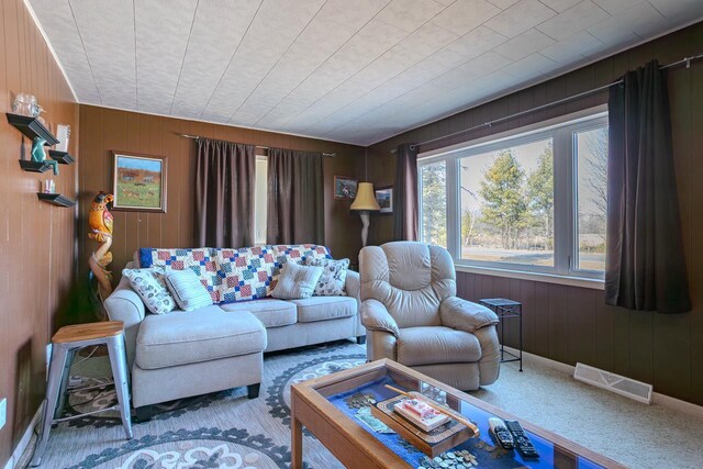 living area featuring carpet floors, baseboards, wooden walls, and visible vents