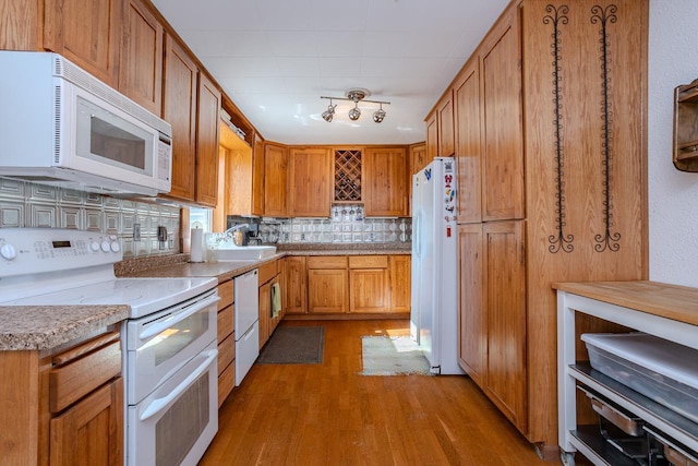 kitchen with backsplash, brown cabinetry, a sink, wood finished floors, and white appliances