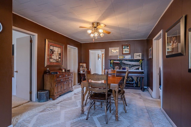 dining area with light carpet, wood walls, and a ceiling fan