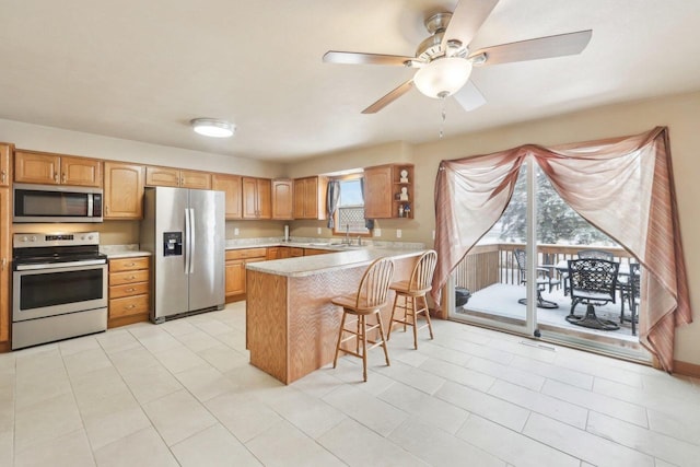 kitchen with light countertops, appliances with stainless steel finishes, ceiling fan, a peninsula, and a kitchen bar