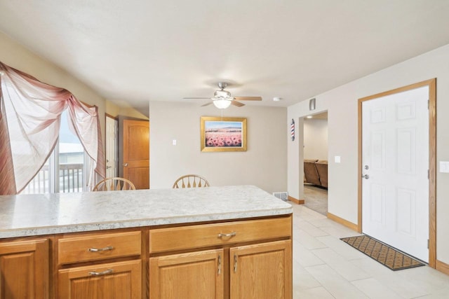 kitchen featuring visible vents, brown cabinetry, baseboards, ceiling fan, and light countertops