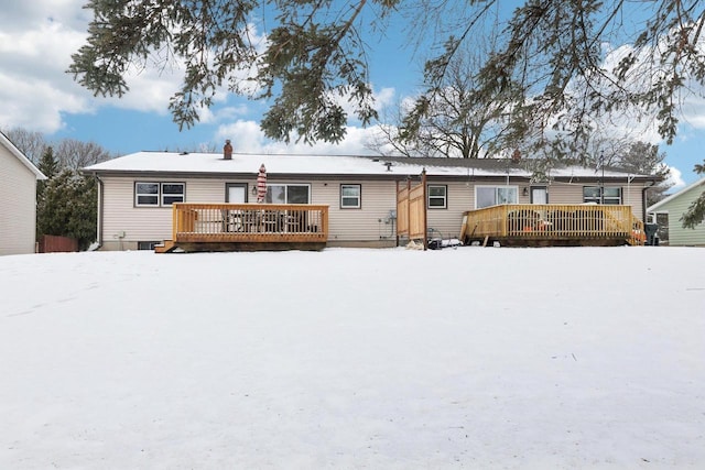 snow covered house featuring a deck and a chimney