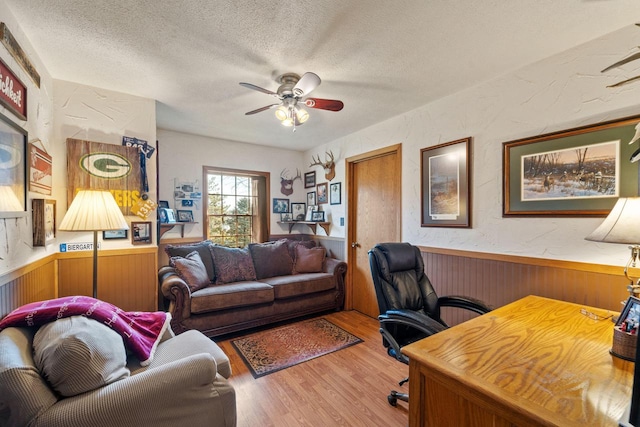 office with a ceiling fan, a textured wall, wainscoting, wood finished floors, and a textured ceiling