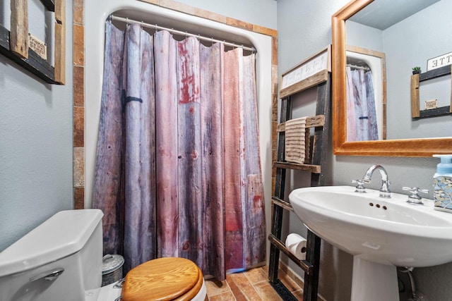 full bath featuring a textured wall, a sink, toilet, and a shower with curtain