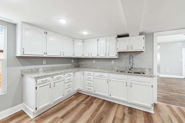 kitchen featuring light wood-type flooring, white cabinetry, a sink, and baseboards