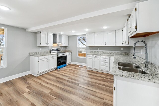 kitchen featuring electric stove, light wood-style flooring, a sink, wall chimney range hood, and baseboards