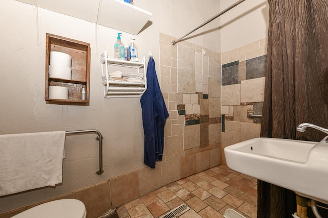 bathroom with stone finish floor, a sink, a tile shower, and toilet