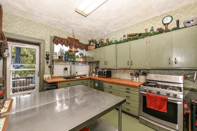 kitchen with stainless steel counters, appliances with stainless steel finishes, a sink, green cabinetry, and wallpapered walls