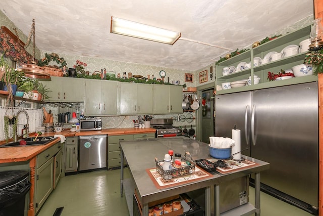 kitchen featuring open shelves, butcher block counters, green cabinets, appliances with stainless steel finishes, and a sink