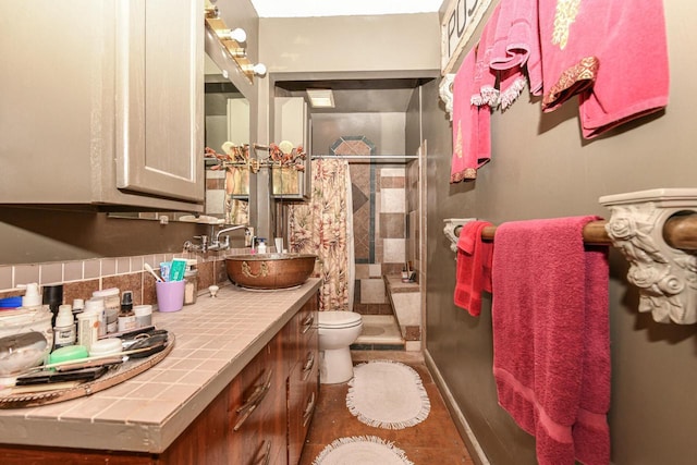 bathroom with toilet, vanity, baseboards, decorative backsplash, and a stall shower