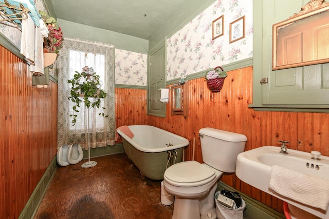 bathroom featuring toilet, a sink, wood finished floors, a freestanding bath, and wainscoting