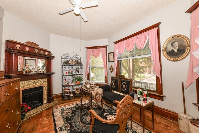 living area featuring baseboards, a ceiling fan, a tile fireplace, wood finished floors, and a textured ceiling