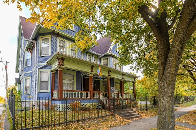 victorian-style house with a porch, a shingled roof, and a fenced front yard