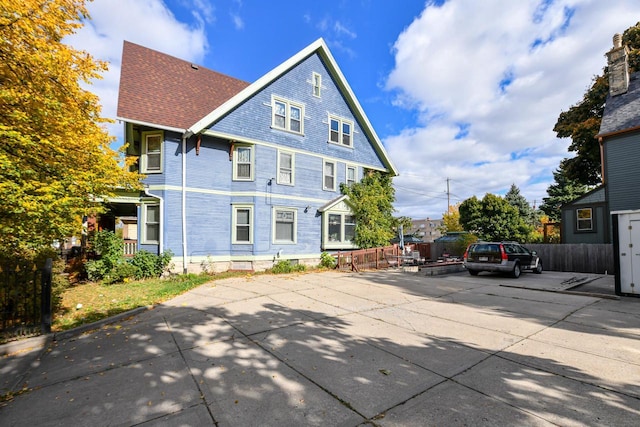 rear view of house featuring a shingled roof and fence