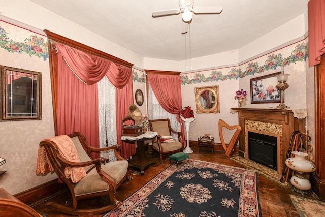 living area featuring a glass covered fireplace, a ceiling fan, and baseboards