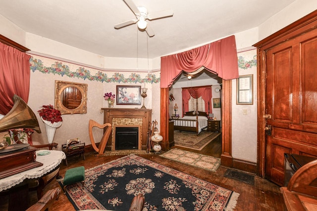 sitting room with dark wood-style floors, ceiling fan, a fireplace, and baseboards