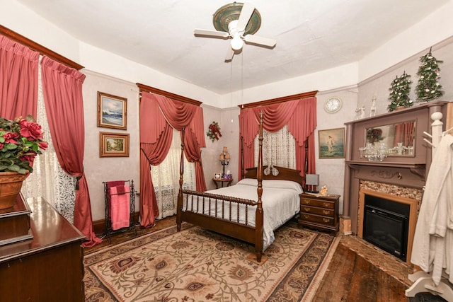 bedroom with ceiling fan, wood finished floors, and a glass covered fireplace