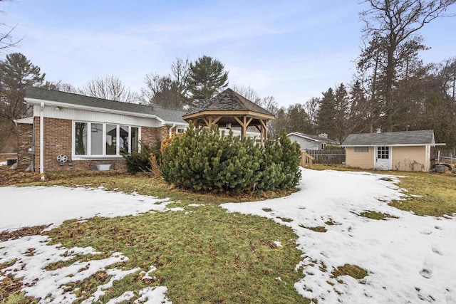 snow covered back of property featuring a gazebo, brick siding, an outdoor structure, and fence