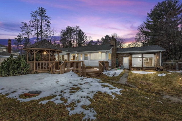 snow covered back of property featuring a wooden deck, a chimney, and a gazebo