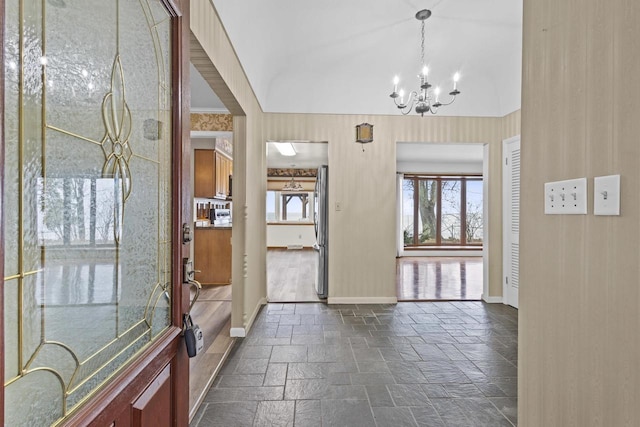 foyer with lofted ceiling, stone tile flooring, baseboards, and an inviting chandelier